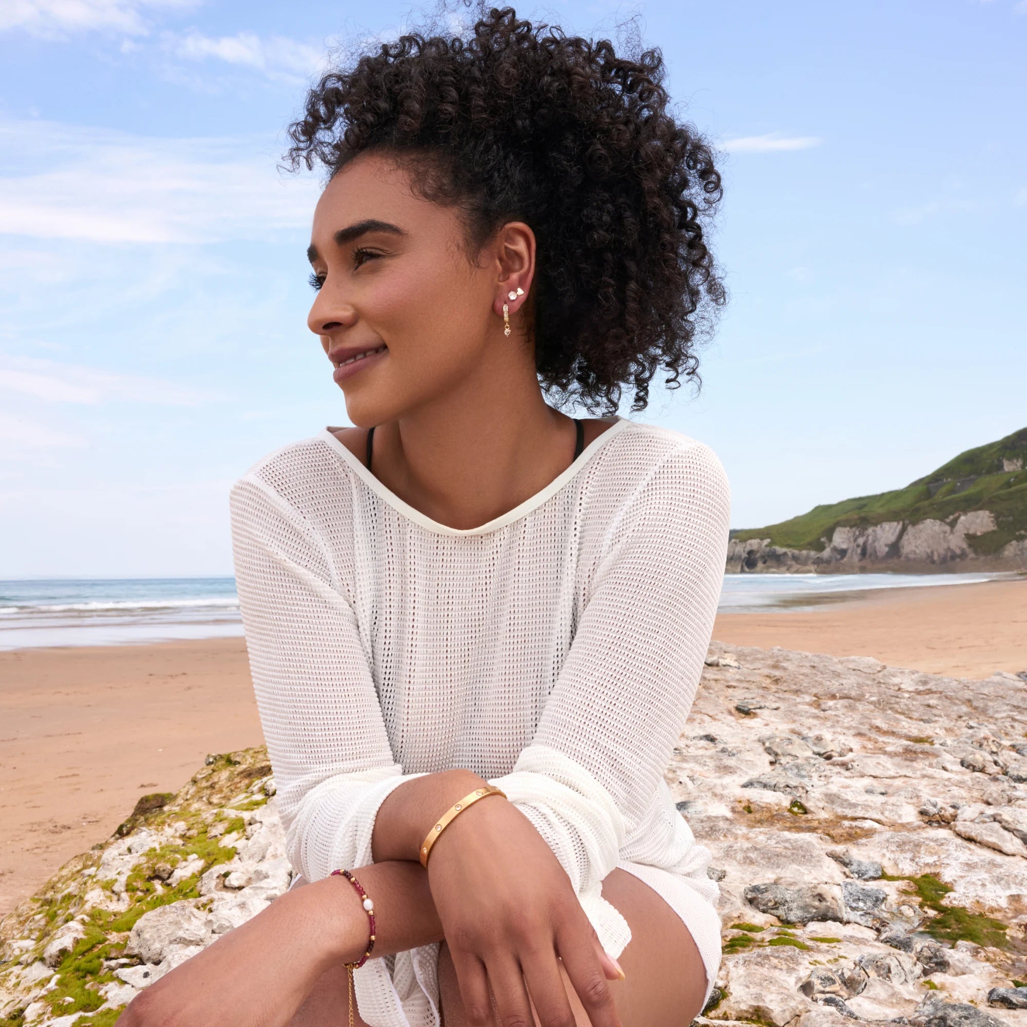 Woman sitting on a rocky beach with ocean and sky in the background