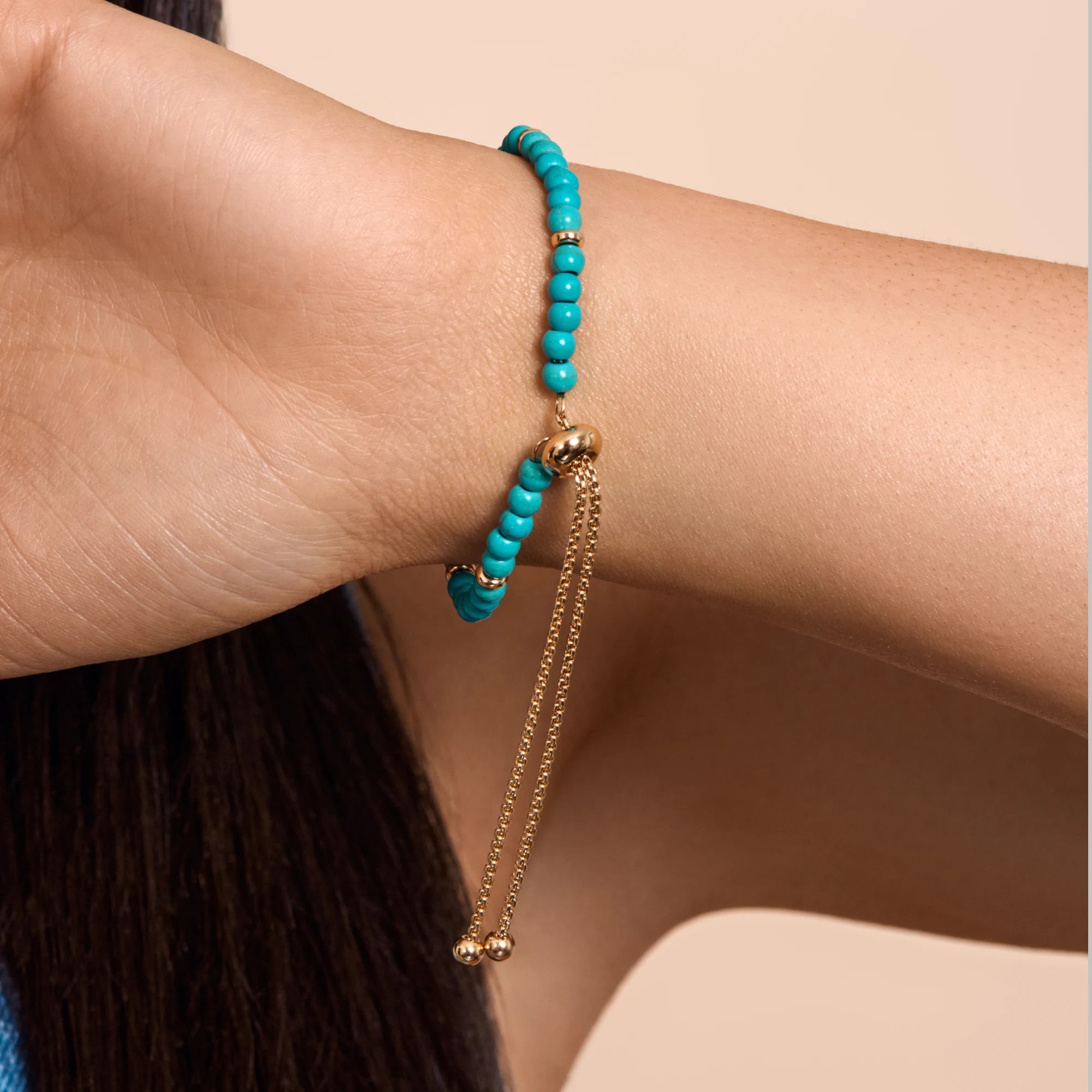 Turquoise beaded bracelet with gold chain on a wrist against a neutral background