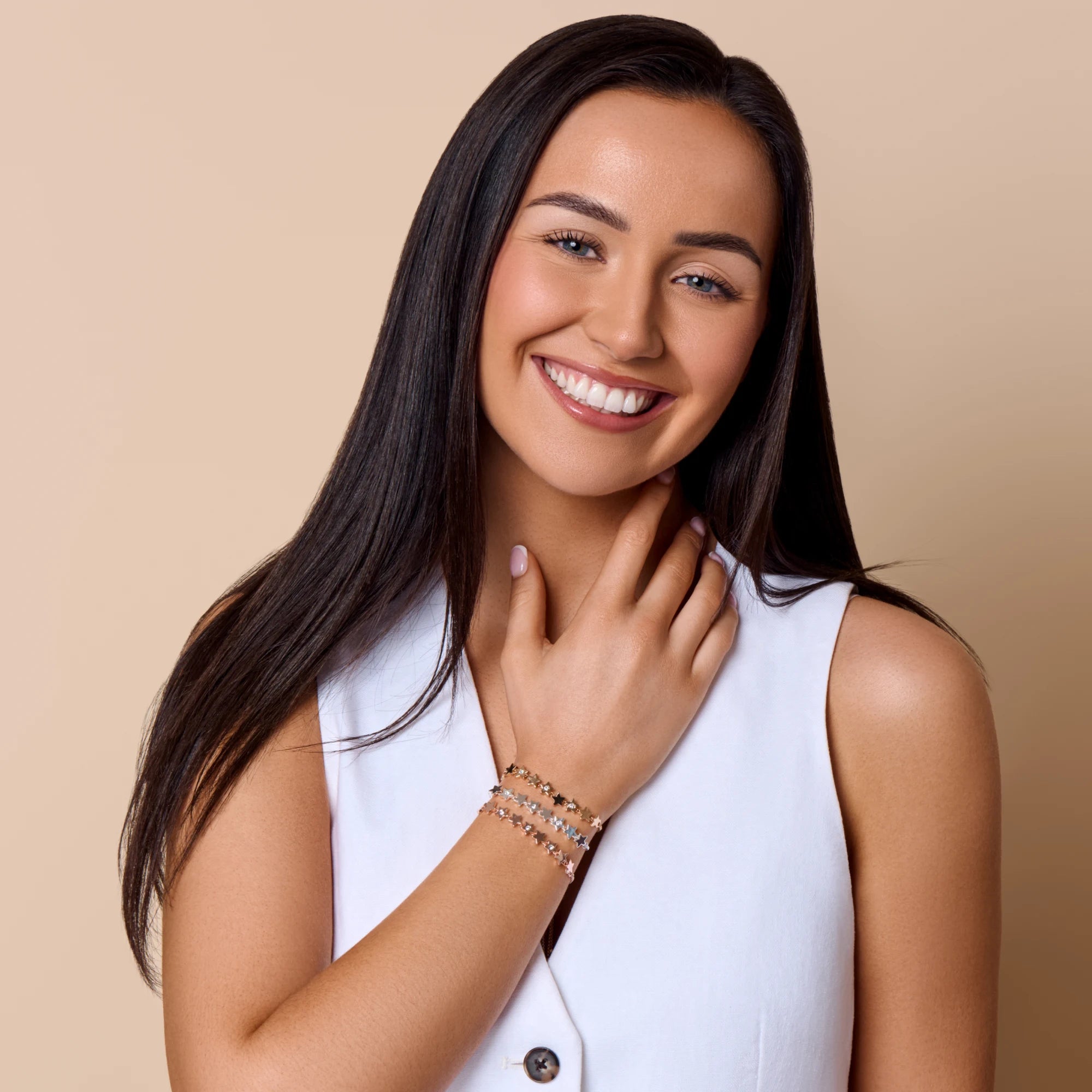 Woman wearing a white sleeveless top and multiple bracelets on a beige background