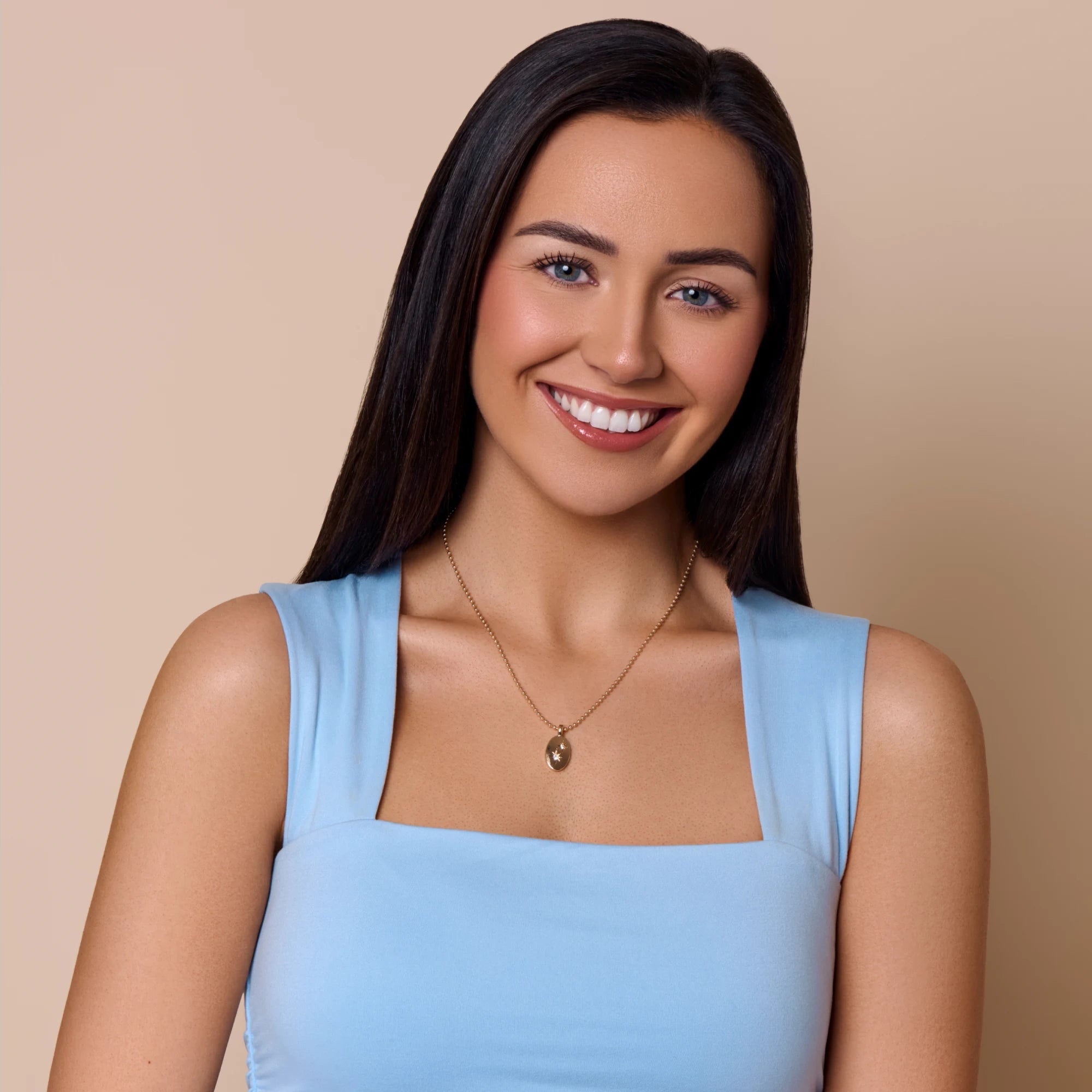 Woman wearing a light blue top and necklace against a beige background
