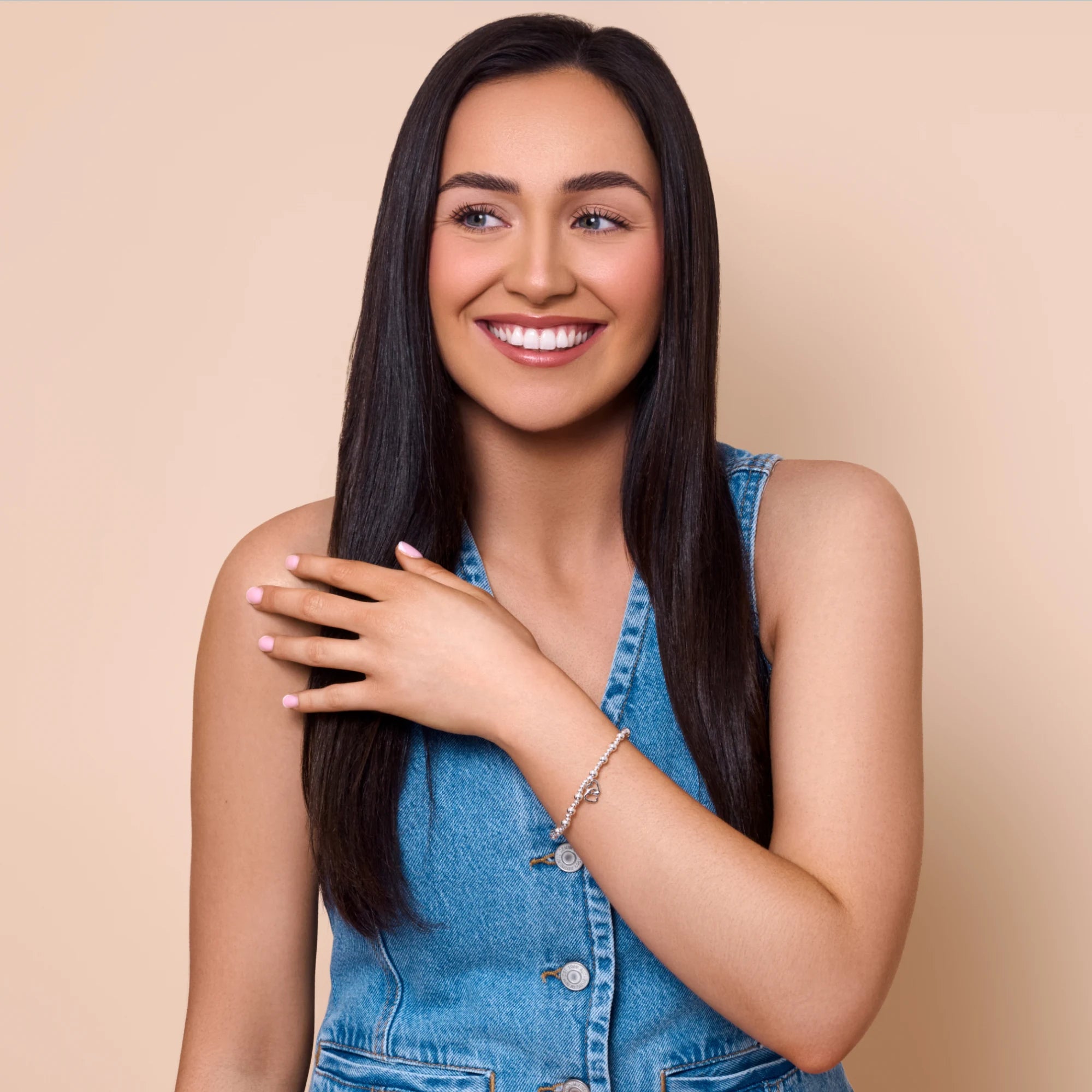 Woman with long dark hair wearing a denim dress against a beige background