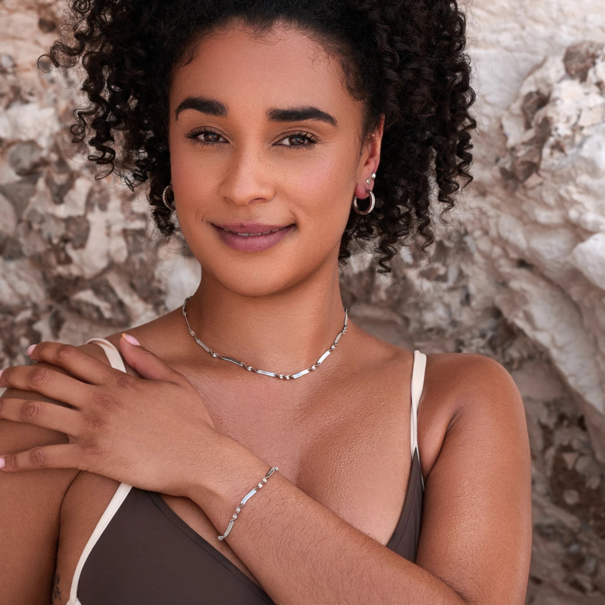 Woman wearing a necklace and bracelet against a textured wall background