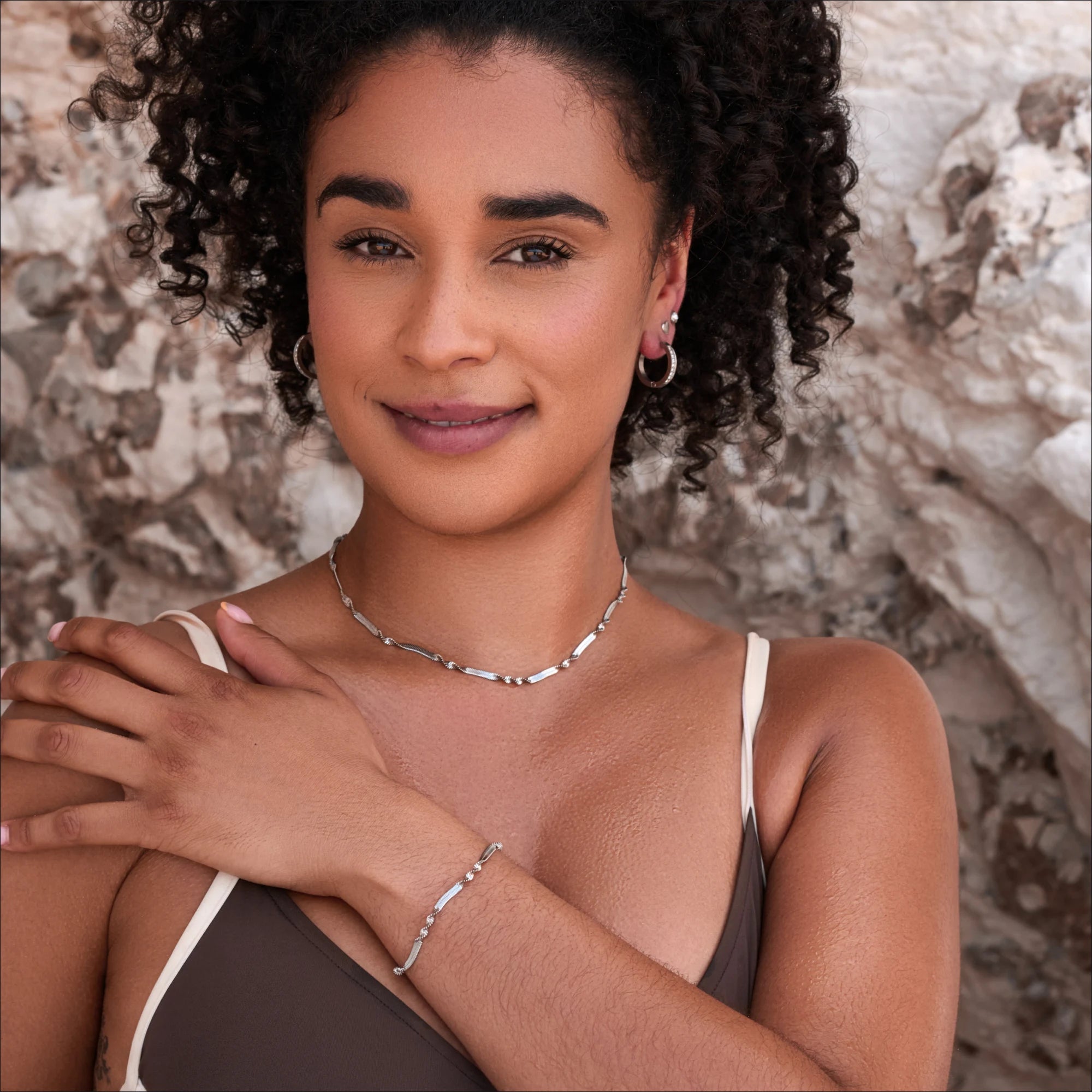 Woman wearing a necklace and bracelet against a textured wall background
