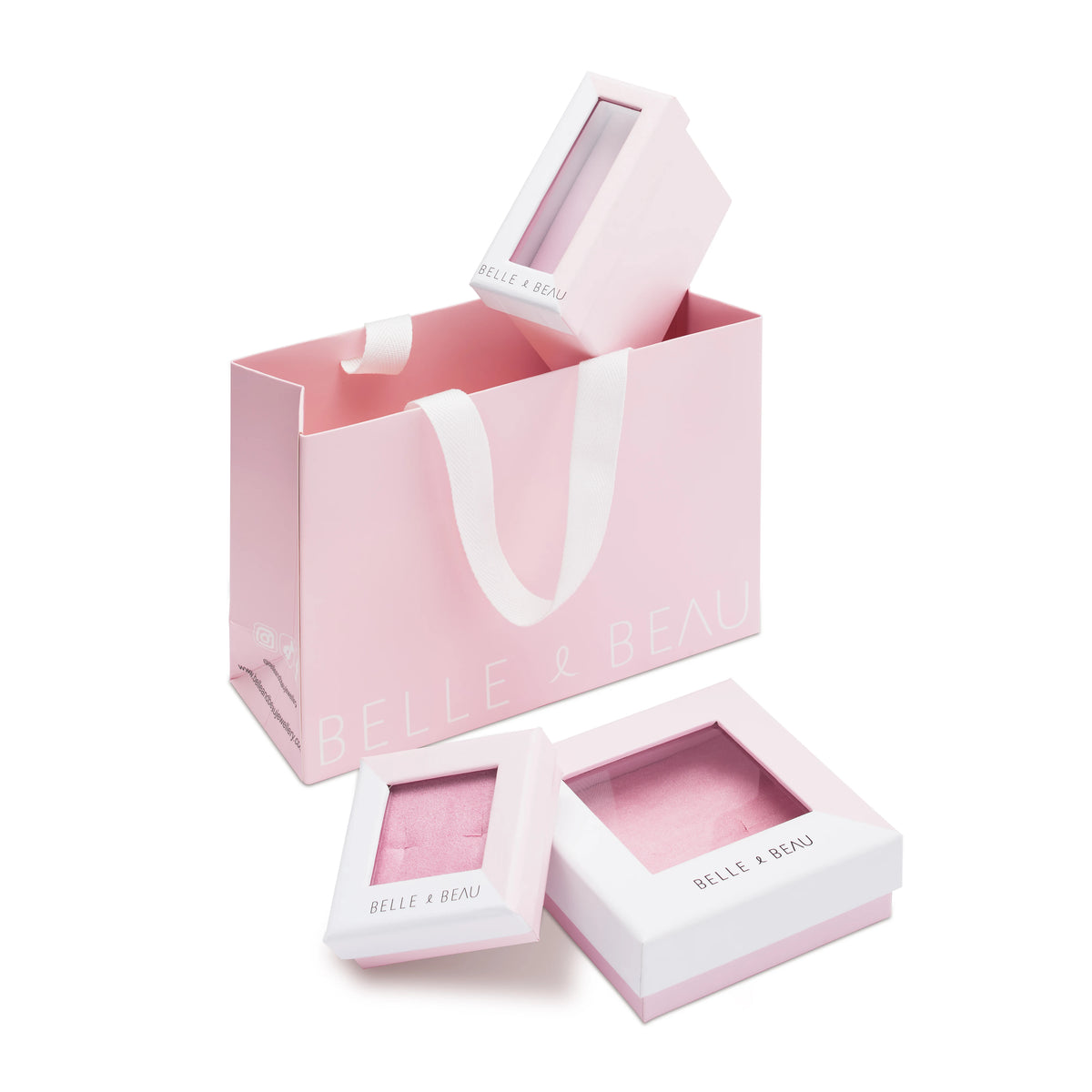 Pink BELLE & BEAU gift set featuring a large pink shopping bag, a square compact with a clear window, and two smaller rectangular boxes with clear windows, all on a white background.