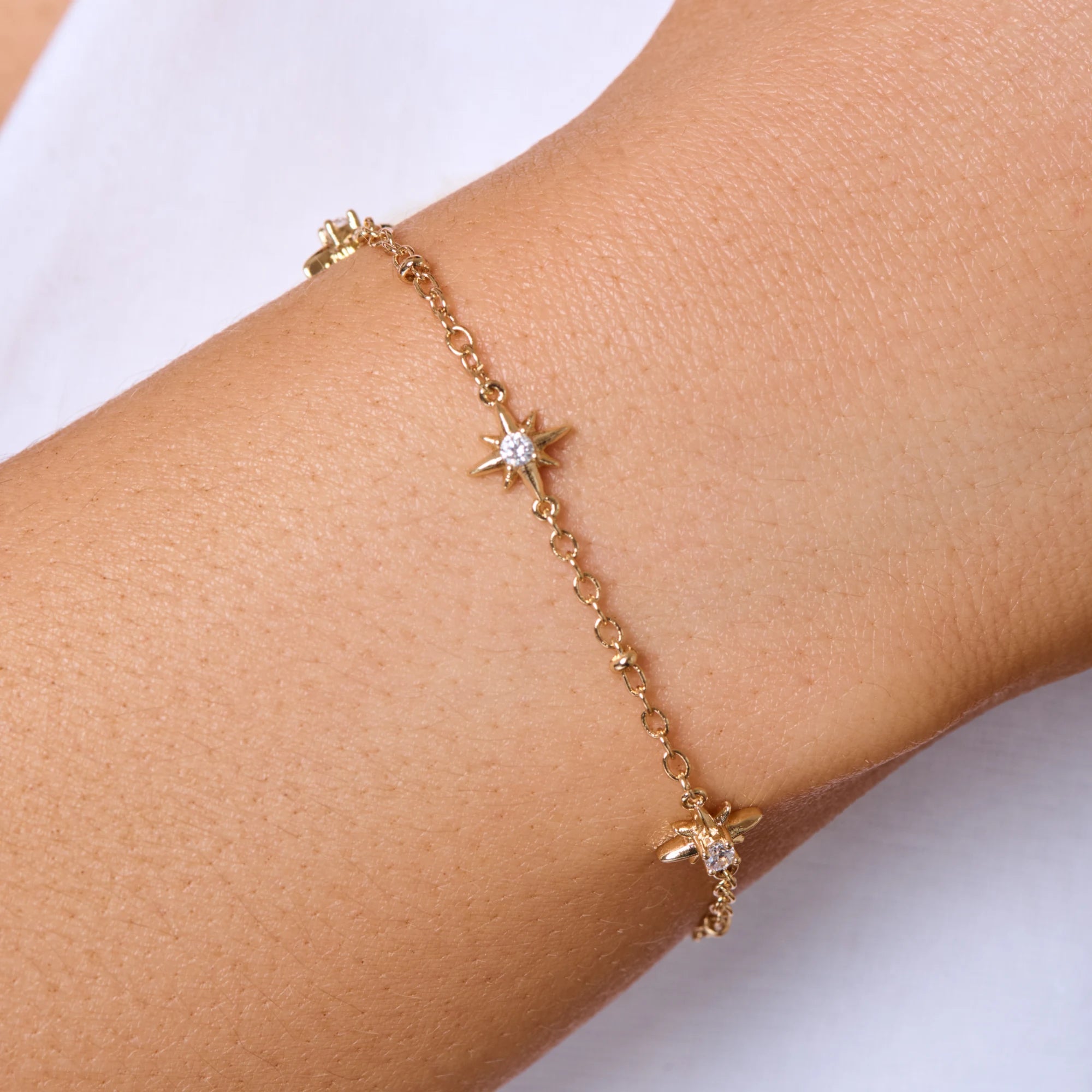 Gold bracelet with star-shaped charms on a wrist against a white background