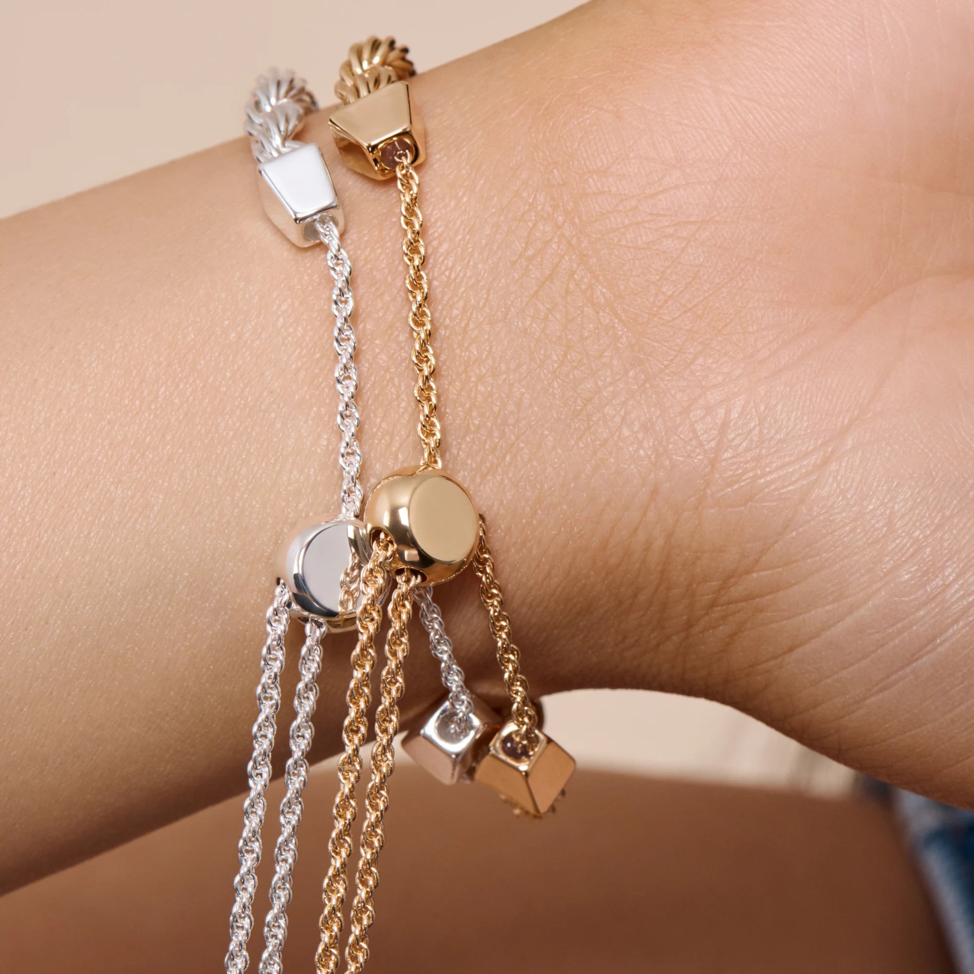 Three gold and silver bracelets on a wrist against a neutral background