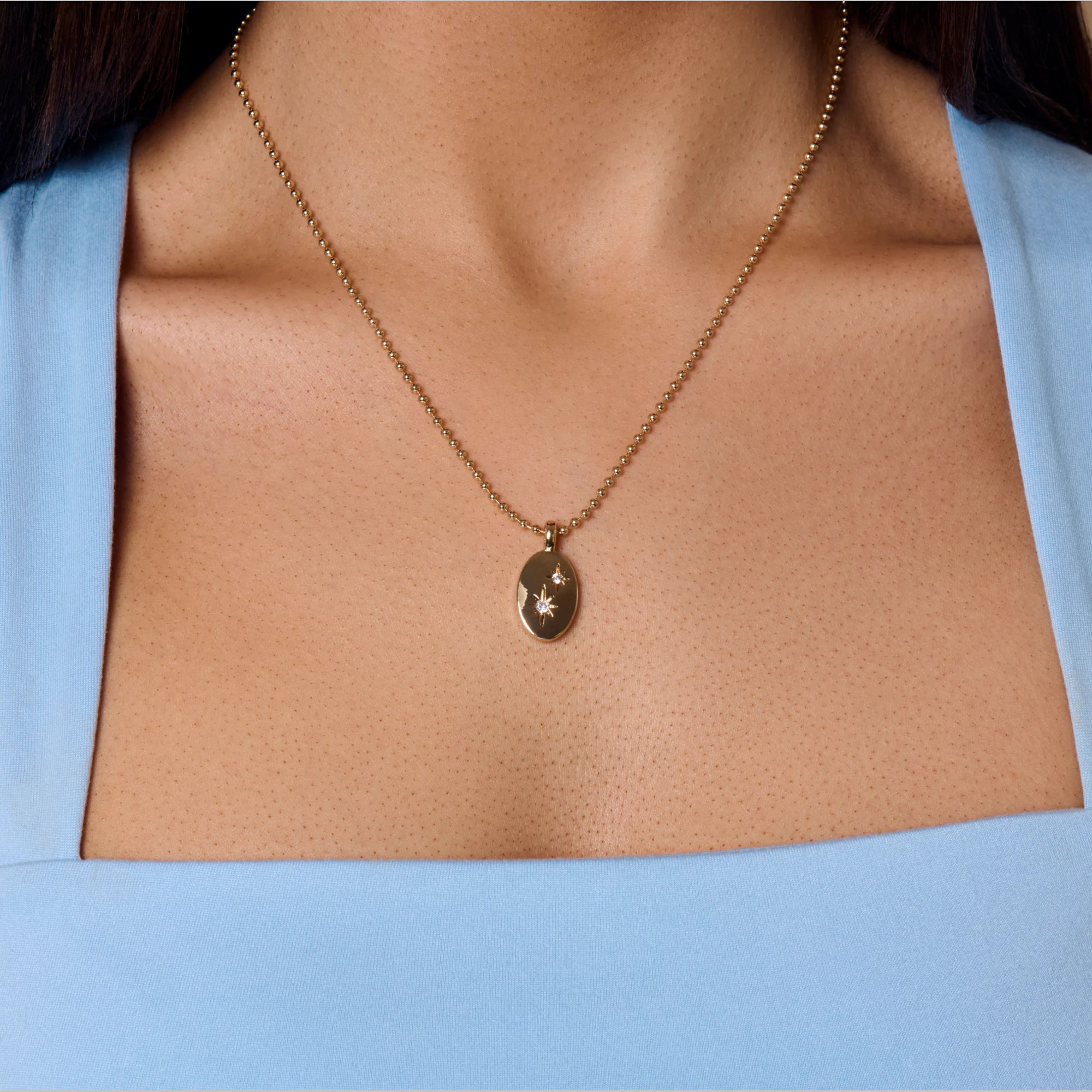 Gold necklace with a pendant on a person wearing a light blue top