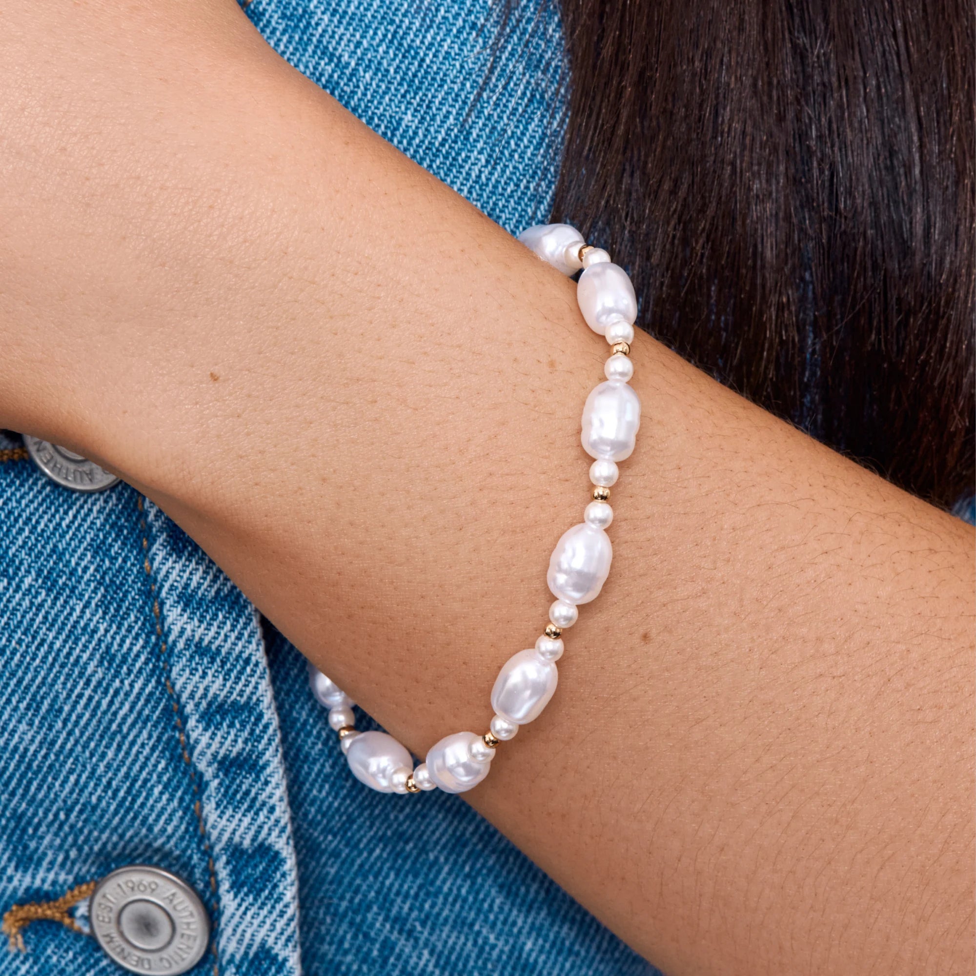 Pearl bracelet on a person's wrist with a denim background