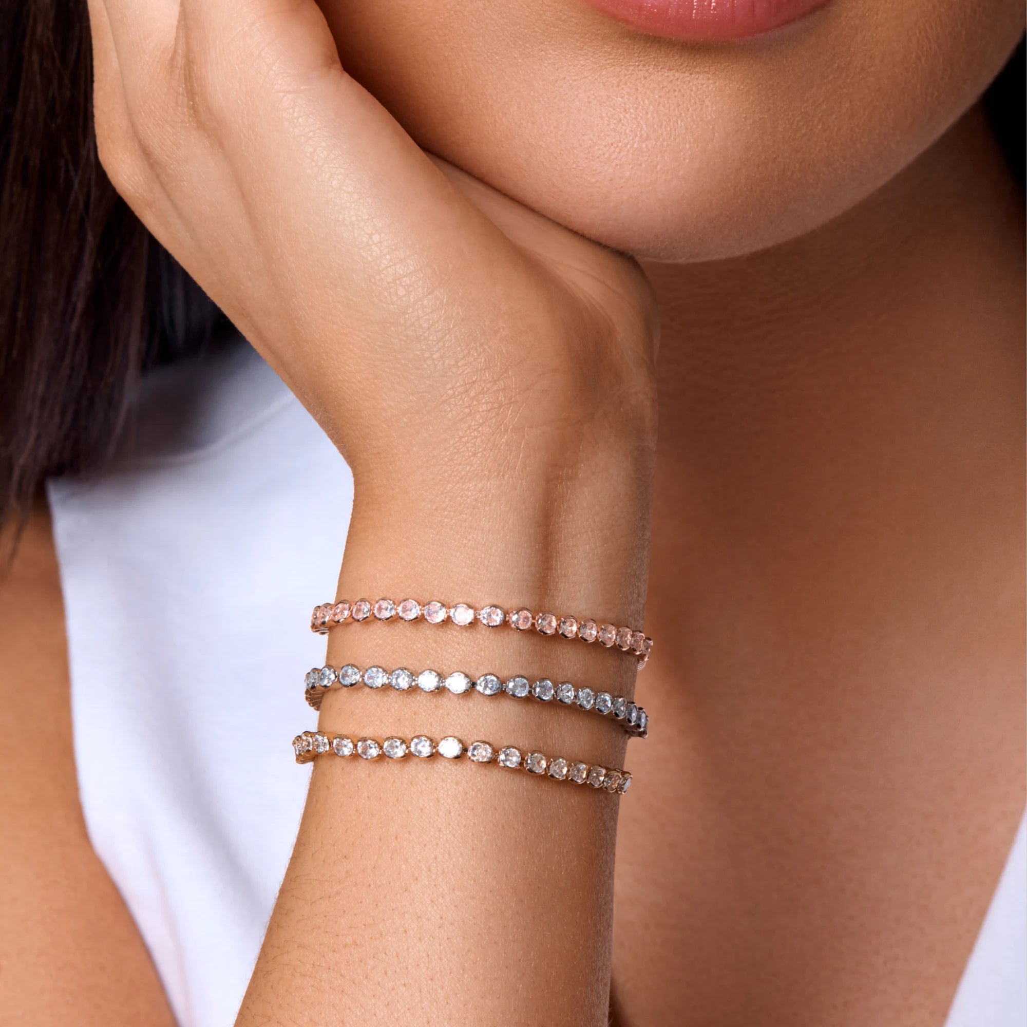 Close-up of a woman's wrist wearing multiple diamond bracelets on a neutral background