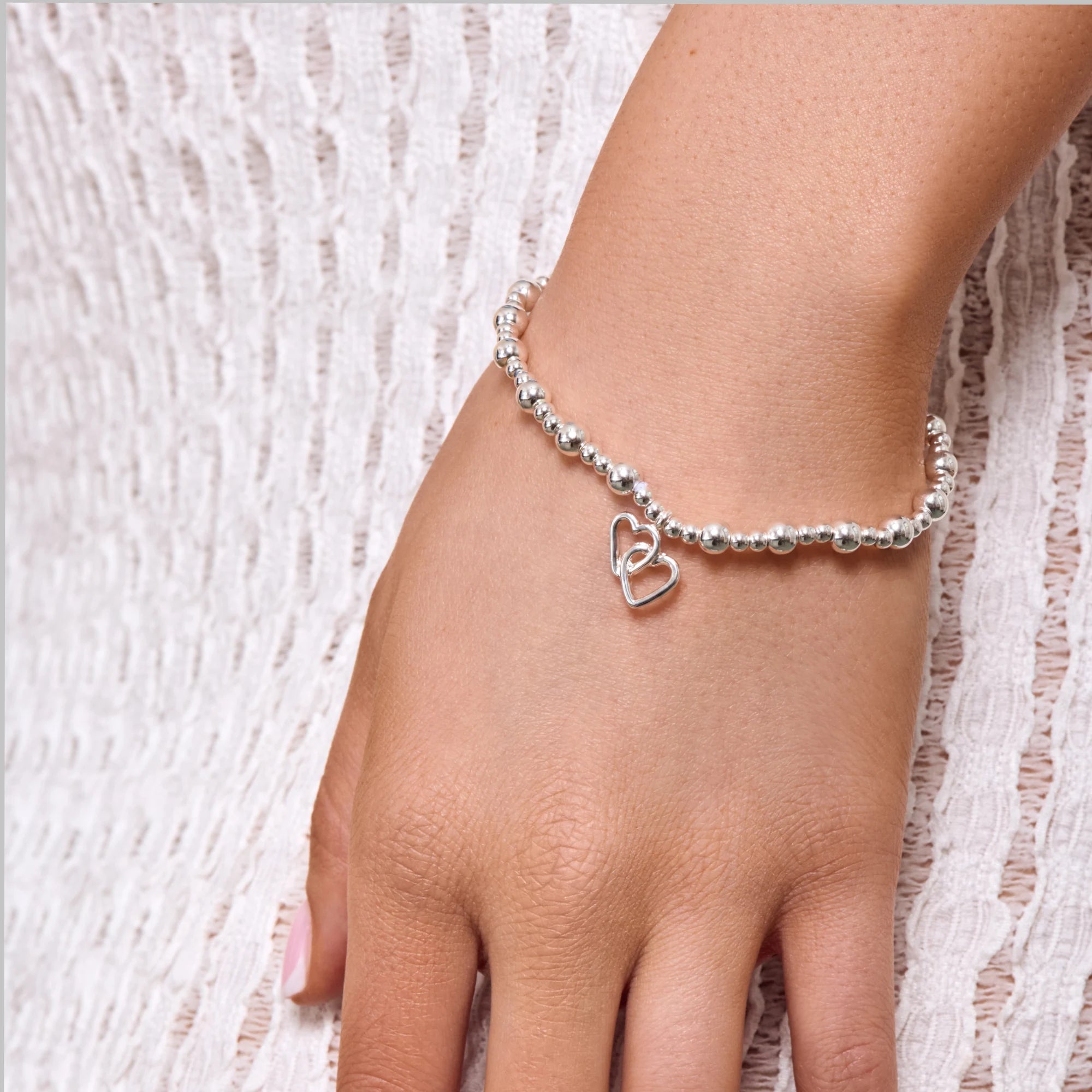 Silver beaded bracelet with a heart charm on a wrist against a textured white background