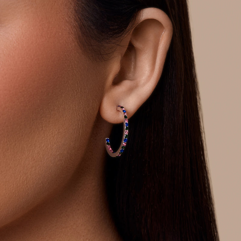 Close-up of an ear wearing a colorful hoop earring against a neutral background