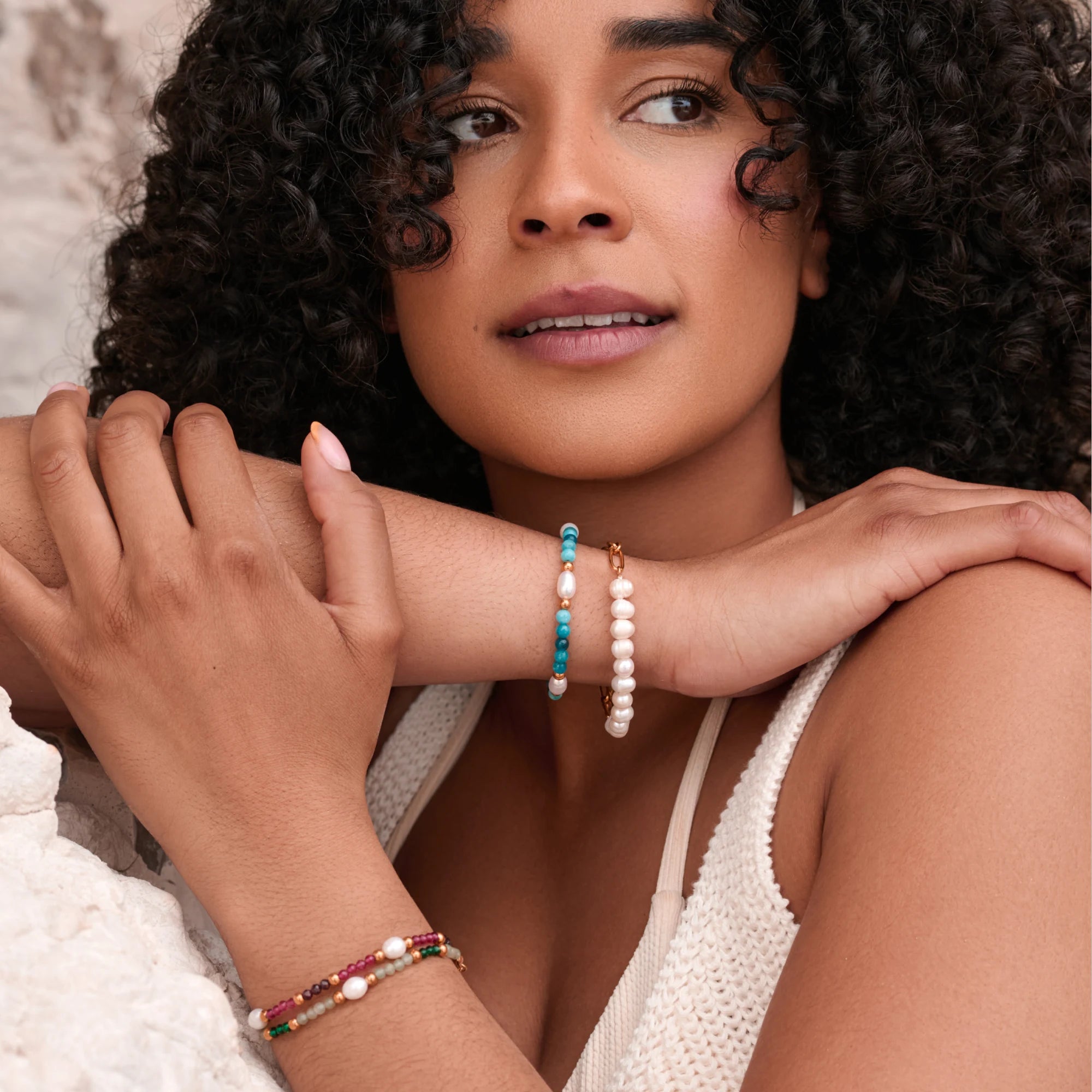 Woman wearing multiple pearl bracelets on a neutral background