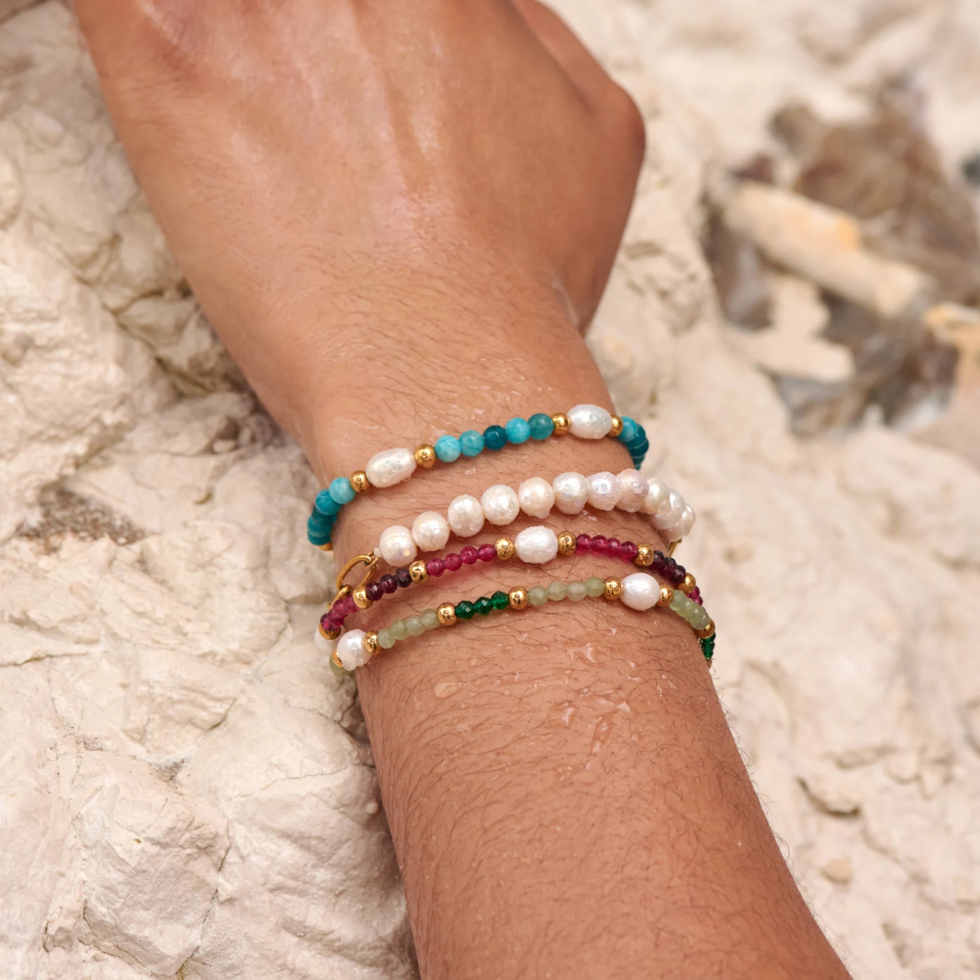 Stack of colorful beaded bracelets on a wrist against a textured stone background