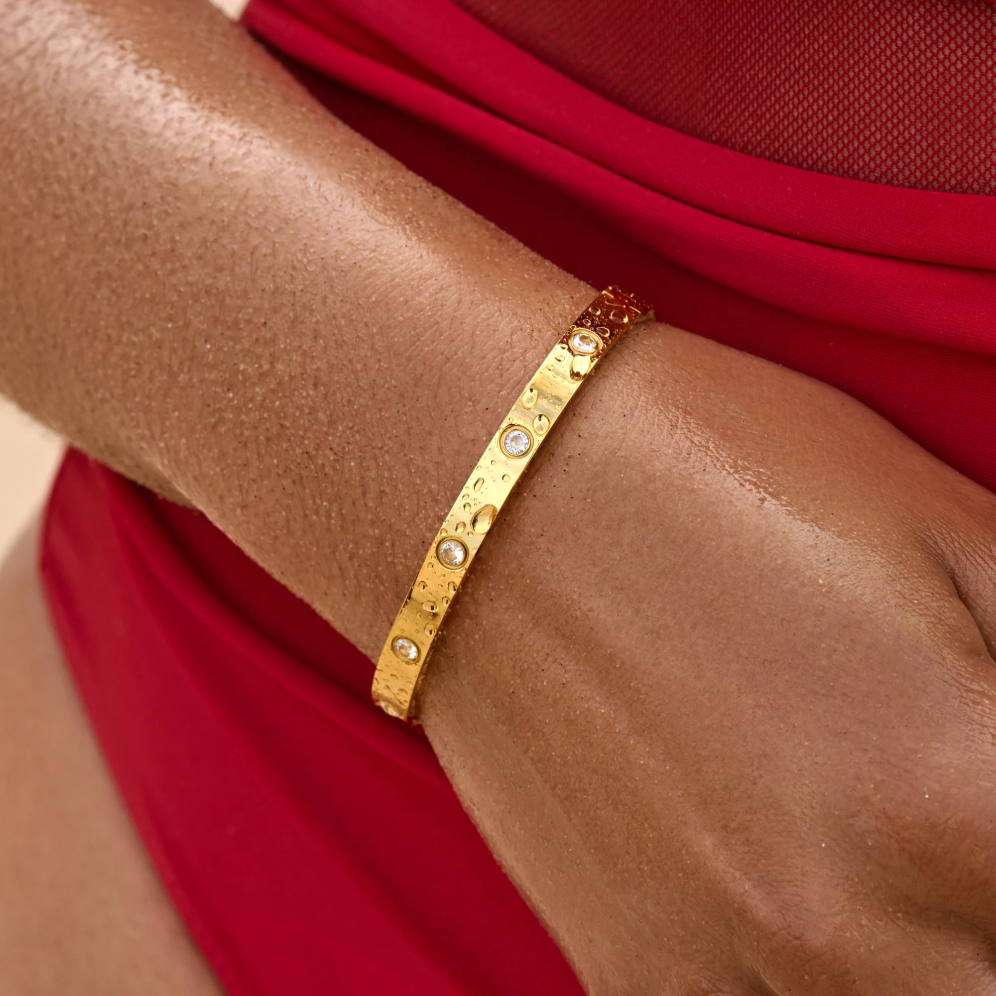 Gold bracelet with small stones on a wrist against a red fabric background