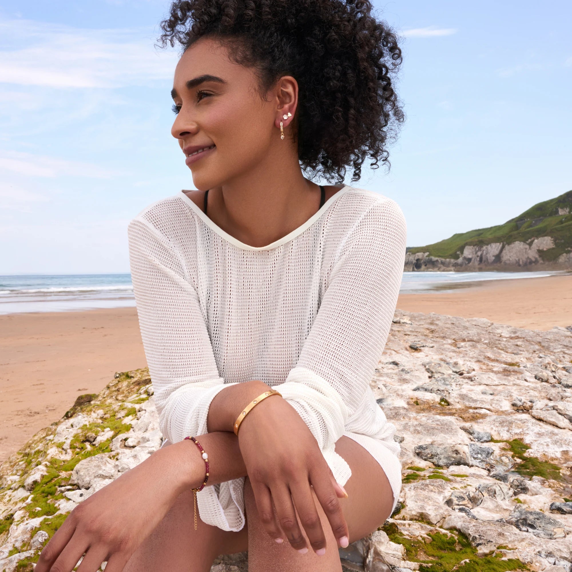 Woman sitting on a rocky beach with ocean and sky in the background