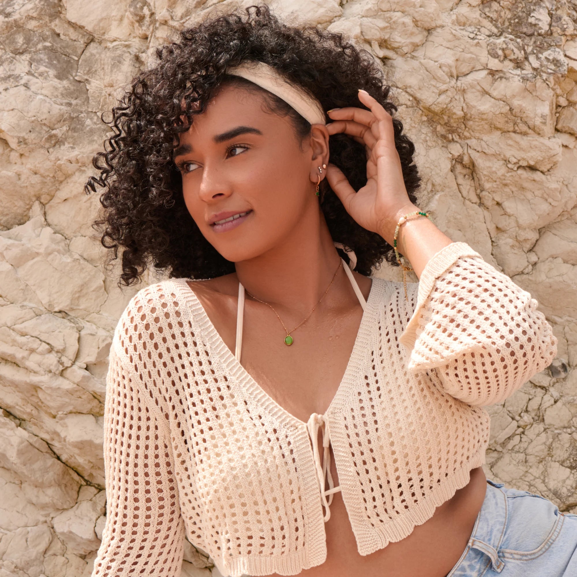 Woman wearing a beige crochet top against a stone wall
